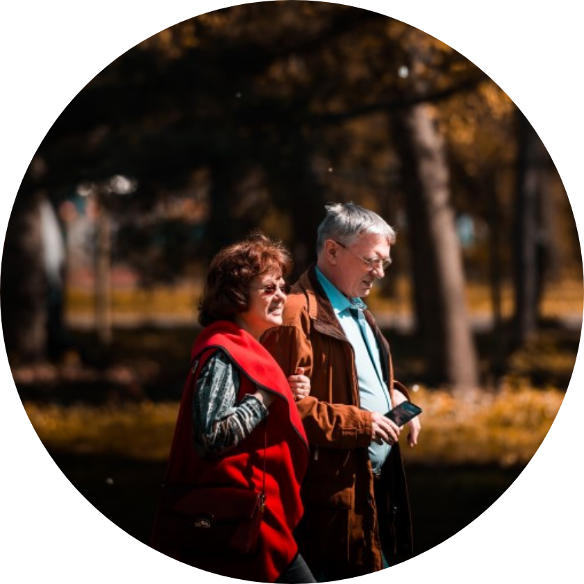Two people of senior age walking through a park with arms entwined
